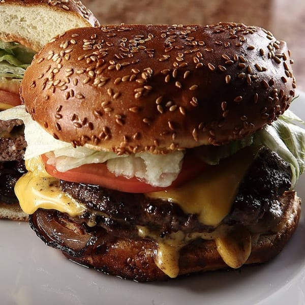A close-up of a double cheeseburger with melted cheese, lettuce, tomato, and a sesame seed bun.