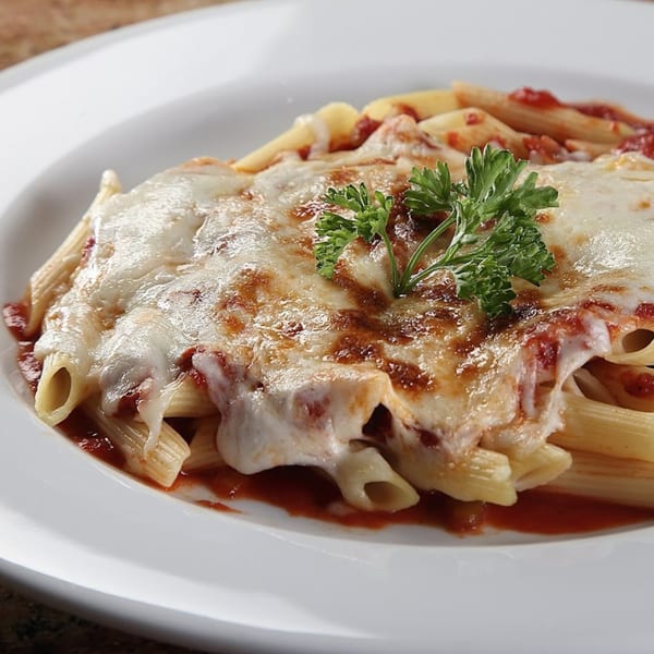 Baked penne pasta with melted cheese, red sauce, and a parsley garnish on a white plate.