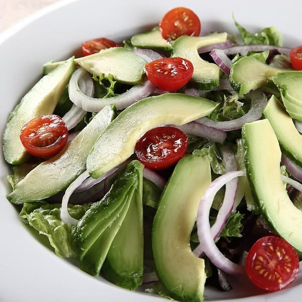 A fresh salad with sliced avocado, red onion, and cherry tomatoes in a white bowl.