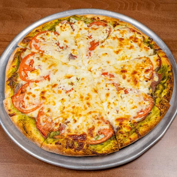 A Chicago's Pizza pesto pizza with sliced tomatoes and melted cheese on a metal pan.