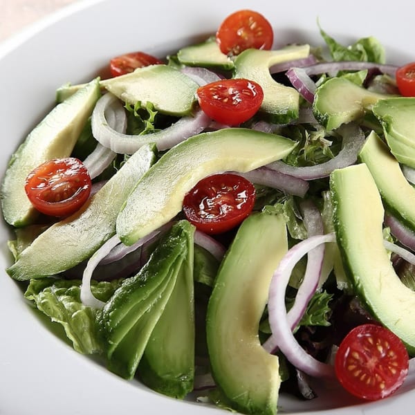 A fresh salad with avocado slices, cherry tomatoes, and red onion on a bed of lettuce.