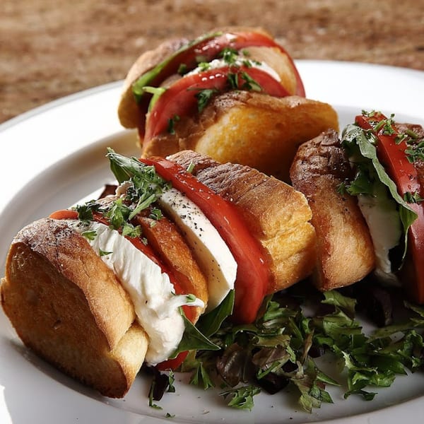 Three caprese sandwiches with fresh mozzarella, sliced tomatoes, and greens on a white plate.
