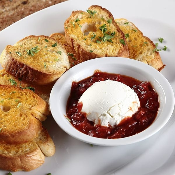 Toasted bread slices with parsley, surrounding a white bowl of ricotta cheese and tomato jam.