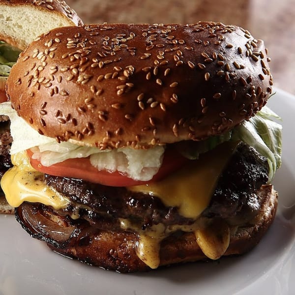 A juicy cheeseburger with melted cheese, lettuce, tomato, and a sesame seed bun on a white plate.