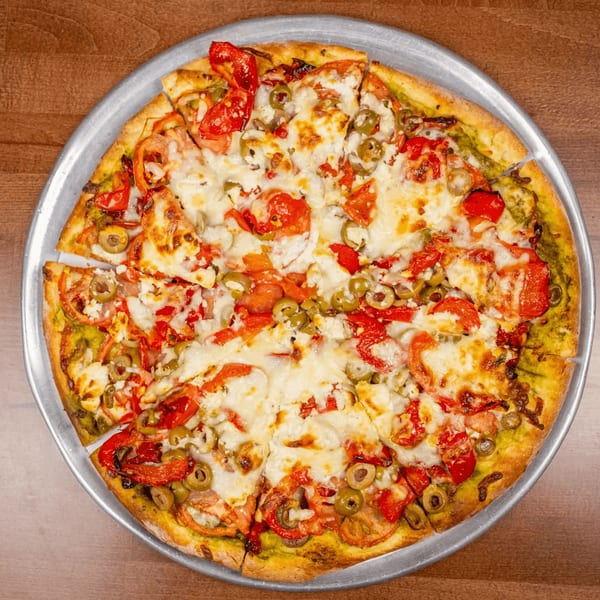 Chicago's Pizza pesto pizza with tomatoes, olives, and feta cheese on a metal pan.