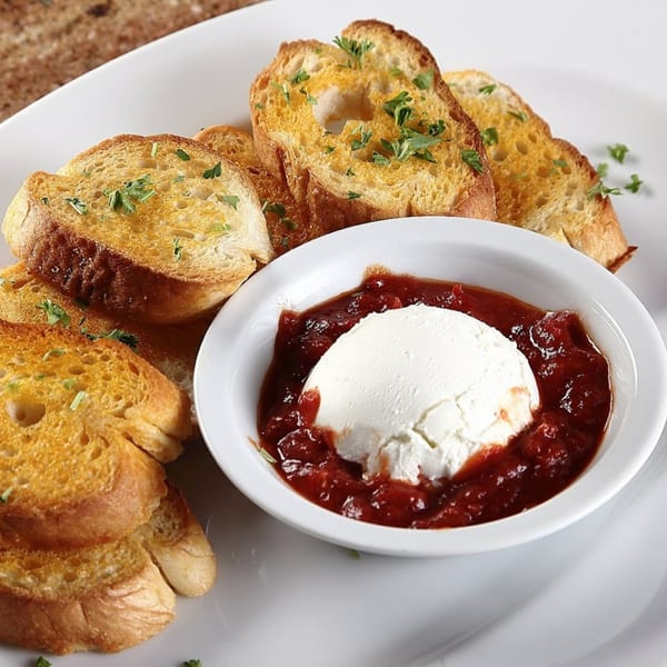 Toasted bread slices with parsley and a white bowl of ricotta cheese in marinara sauce.
