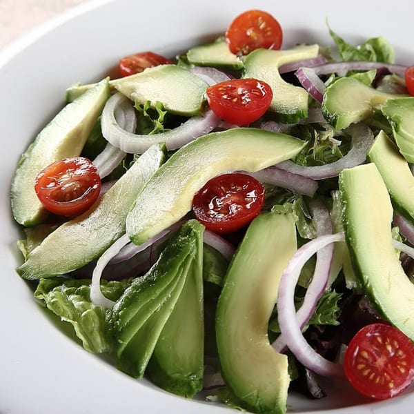 Fresh salad with sliced avocado, red onion, cherry tomatoes, and green lettuce in a white bowl.