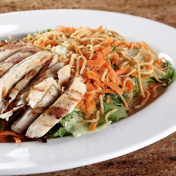 Grilled chicken salad with shredded carrots, crispy noodles, and green lettuce on a white plate.