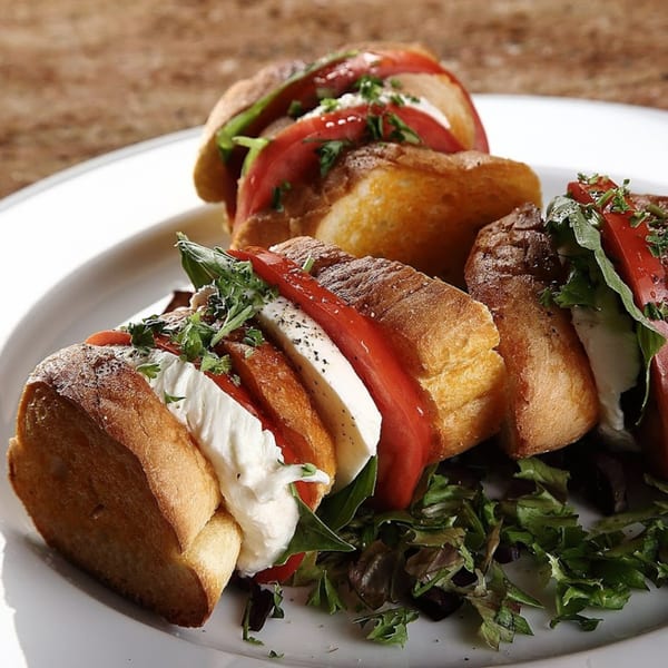 Three Caprese sandwiches with fresh mozzarella, tomatoes, and basil on toasted bread, served with greens.