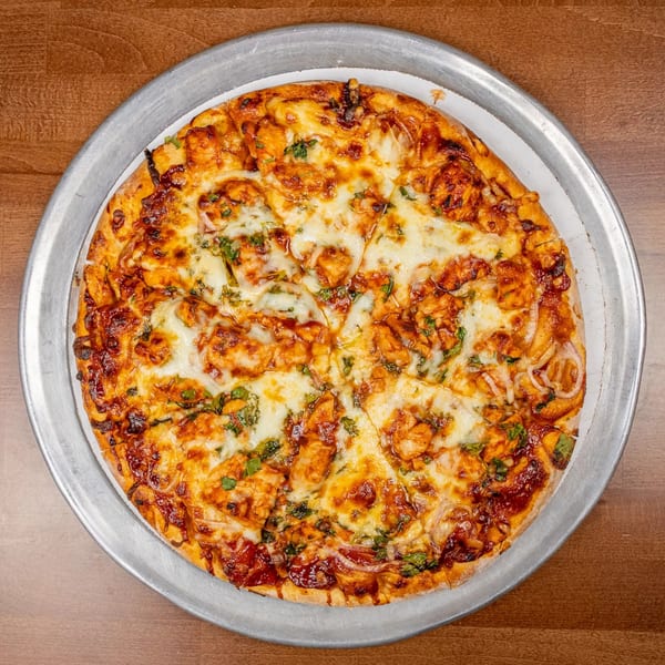 A Chicago's Pizza chicken pizza, topped with melted cheese, red onions, and cilantro, on a metal pan.