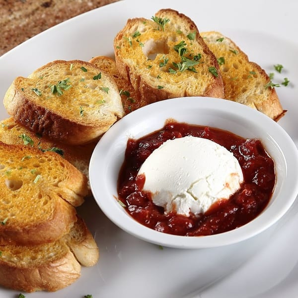 Toasted bread slices with parsley and a white bowl of ricotta cheese with red sauce.